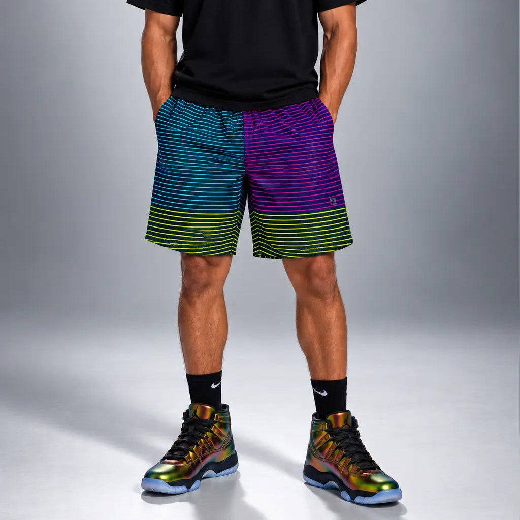 A male model stands against a gray studio background wearing a black crew-neck t-shirt, multicolor striped athletic shorts, black crew socks, and colorful high-top sneakers.