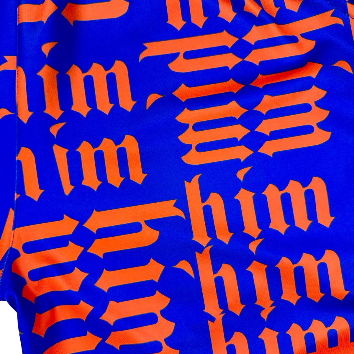 Close up view of texture of Purple soft dry fit shorts with repeating orange him text pattern on a white background