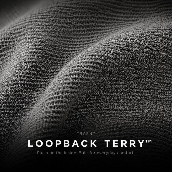 Close-up of dark gray loopback terry fabric with a textured knit surface and soft folds, with the text 'TRAPN LOOPBACK TERRY' and a smaller tagline at the bottom.