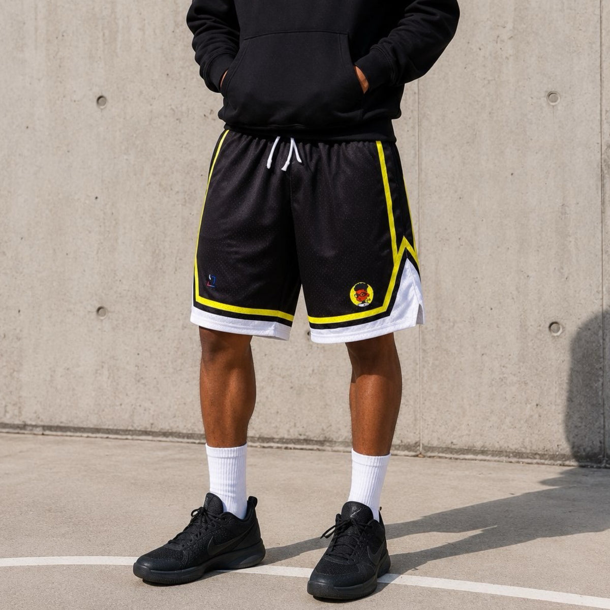 Person wearing black shorts with yellow and white accents, standing against a concrete wall.