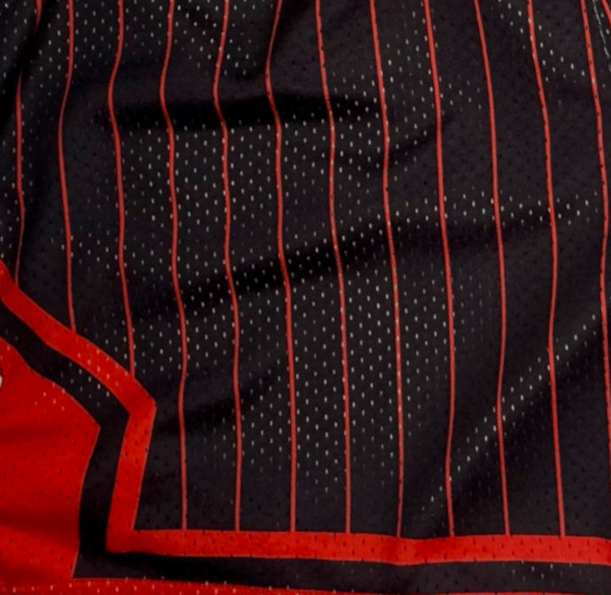 Close-up of a black mesh athletic jersey with thin red vertical pinstripes and a red border along the lower left edge.