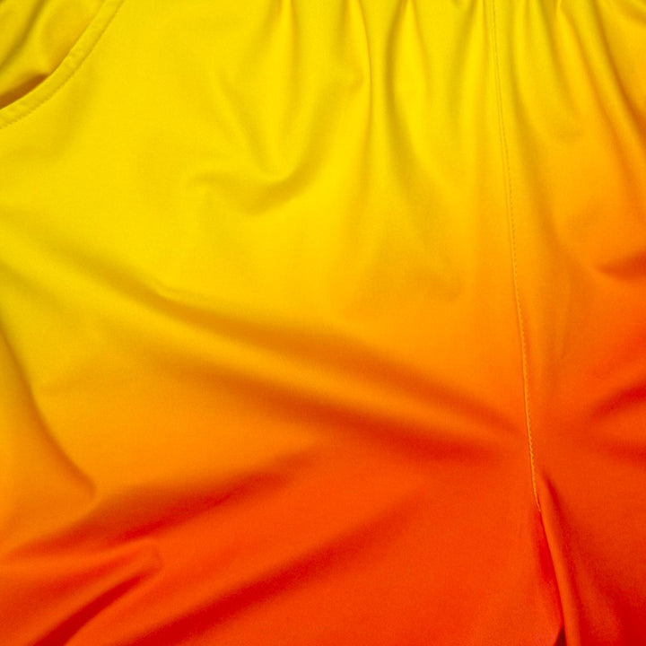 Close up texture view of Sunburst yellow to pink gradient dry fit shorts with yellow stripe on white background.
