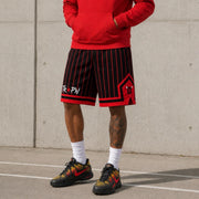 Person wearing red hoodie, black and red striped shorts, and colorful sneakers against a concrete wall.