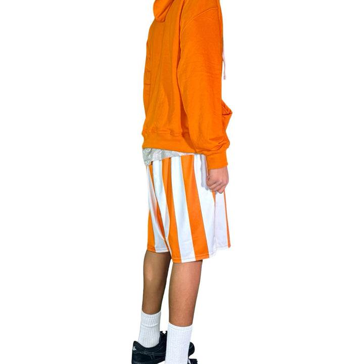 Person wearing an orange hoodie and striped shorts on a white background