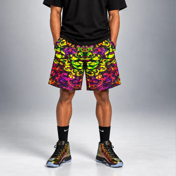 A man modeling a black t-shirt and vibrant multicolor patterned athletic shorts, paired with black Nike socks and colorful sneakers, against a gray studio background.