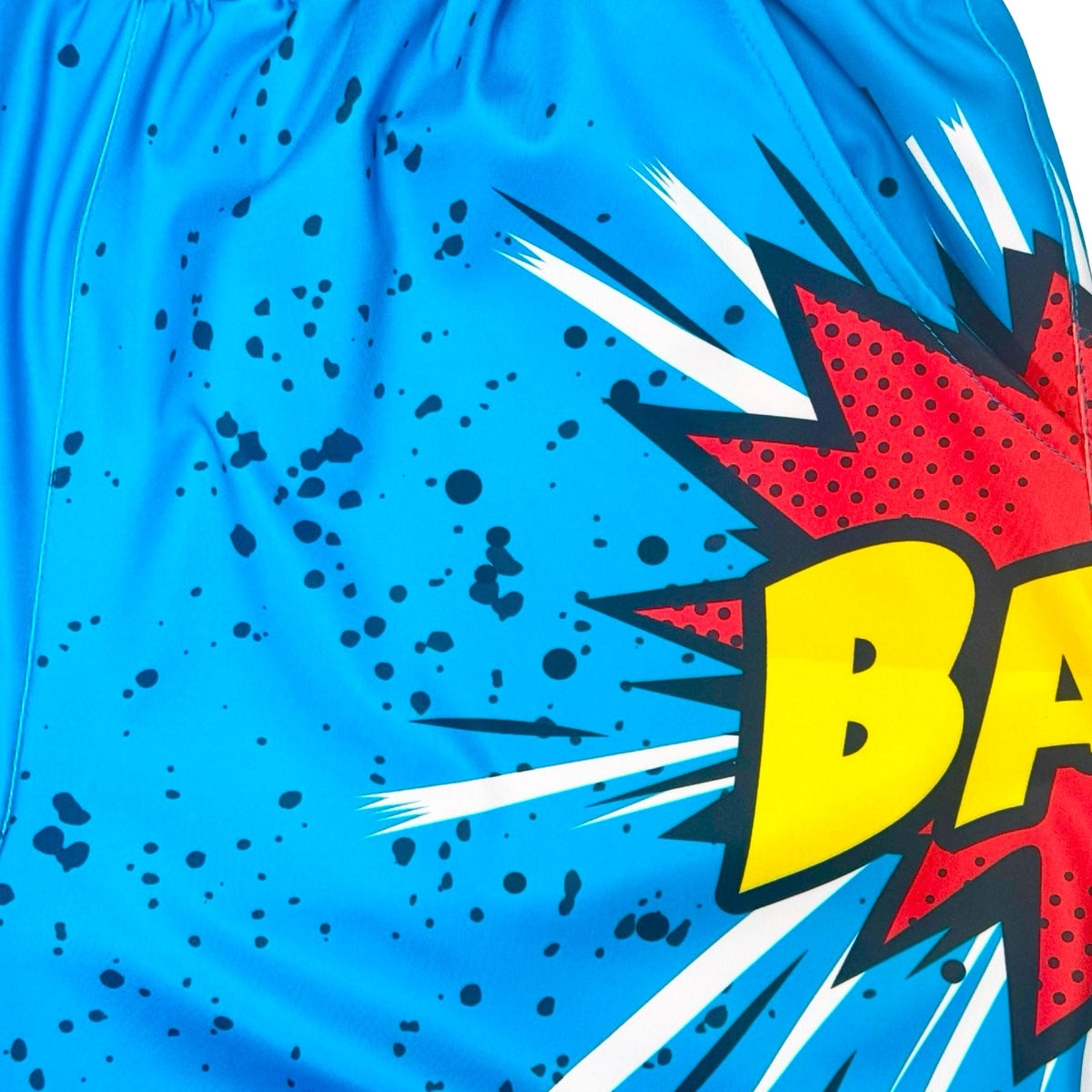 Blue dry fit shorts with a 'BANG!' graphic and black speckles texture closeup
