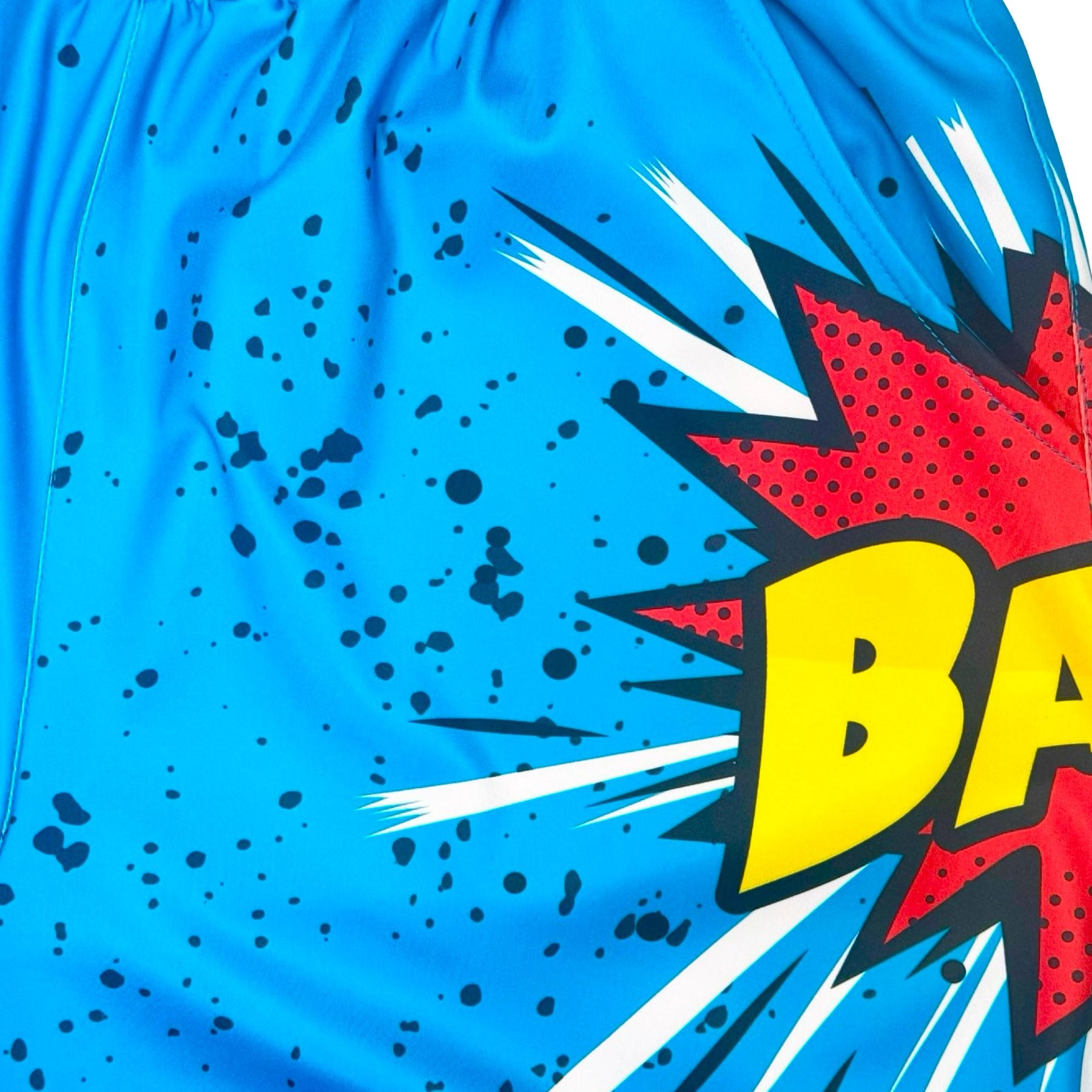 Blue dry fit shorts with a 'BANG!' graphic and black speckles texture closeup