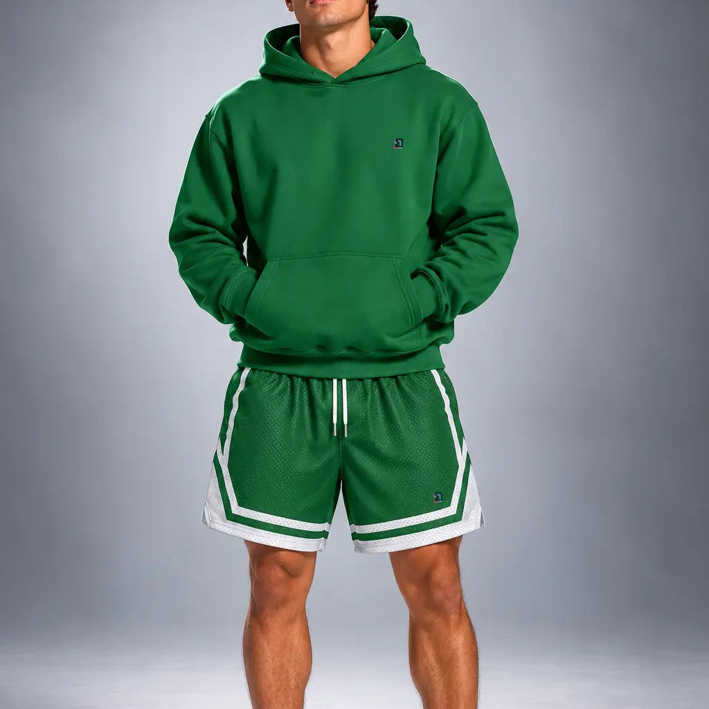 A man modeling a matching green athletic hoodie and shorts set with white trim, paired with white socks and green sneakers, against a gray studio background.