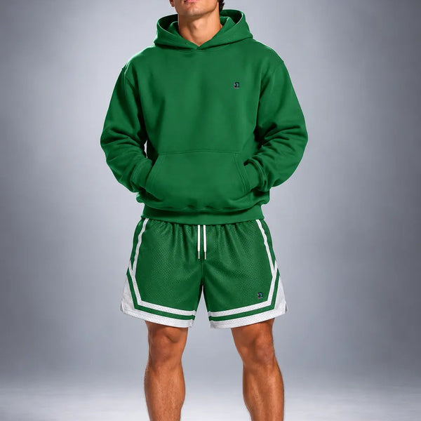 A man modeling a matching green athletic hoodie and shorts set with white trim, paired with white socks and green sneakers, against a gray studio background.
