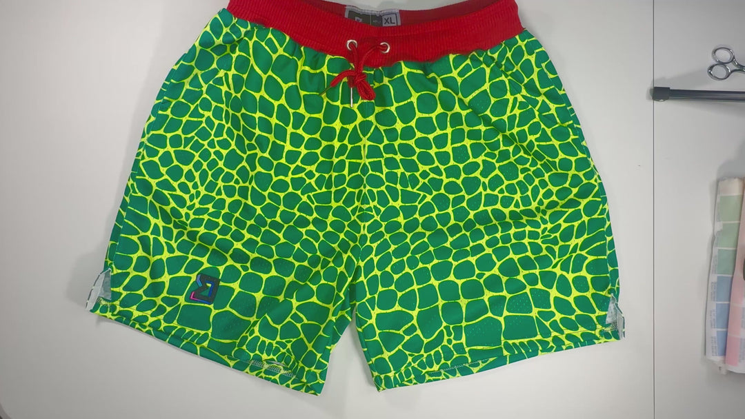 Trap Grinch Mesh Pro basketball shorts with neon green reptile pattern, red pro waistband, and zippered pockets by Trap’N Shorts.
