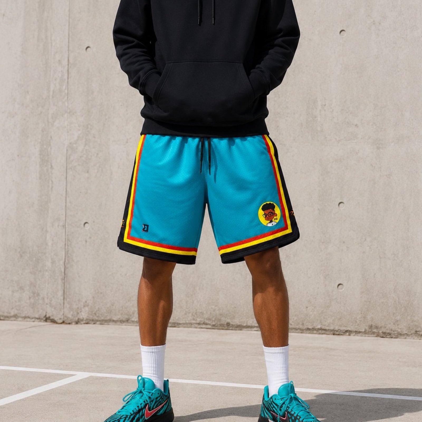 Person wearing blue shorts with a colorful border and black hoodie on a concrete background